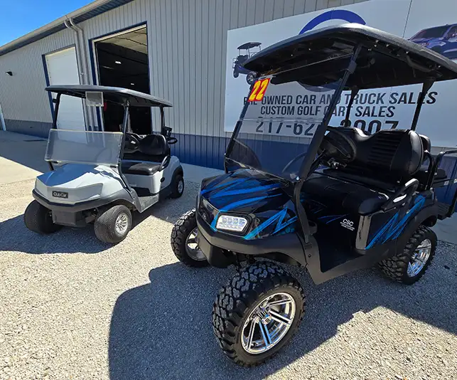 Before and After - Black and blue custom golf cart with off-road tires next to a silver Club Car at CSC Motor Company in Springfield, IL