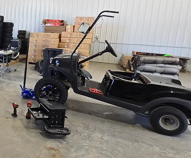 Black golf cart frame in mid-build on shop floor with parts and tires in background – CSC Motor Company Springfield, IL